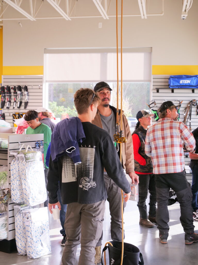 Customers inside a Vermeer Southeast equipment store, interacting and examining arborist gear. Individuals are engaged in conversation, with climbing ropes and arborist supplies visible on display racks in the well-lit store.